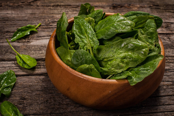 Spinach in a wooden plate on a wooden background - Фото, изображение