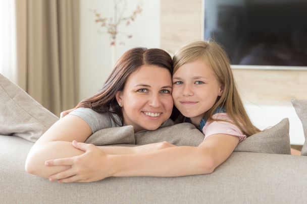 Menschen und Familienkonzept - glücklich lächelndes Mädchen mit Mutter, die sich zu Hause auf dem Sofa umarmt - Foto, Bild