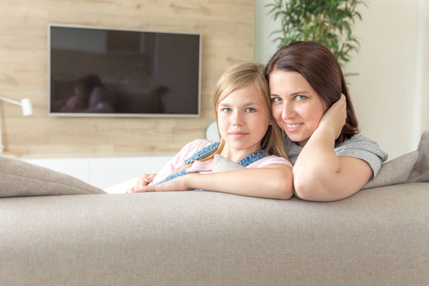 people and family concept - happy smiling girl with mother hugging on sofa at home - Fotoğraf, Görsel