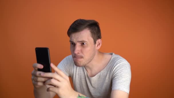 a man shoots a video on the phone on an orange background - Materiaali, video