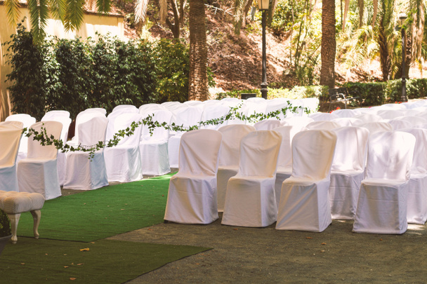 木陰の公園の外で結婚式のイベントでゲストのための白いケープの椅子の列, 天蓋の下のロマンチックな場所 - 写真・画像