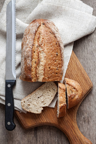 Ρολό ψωμιού ολικής άλεσης με φέτες σε ξύλινη σανίδα στην κουζίνα - Φωτογραφία, εικόνα