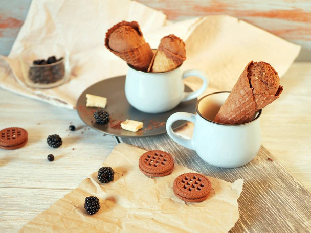 Chocolate ice cream in wafer cones, cookies, berries on a wooden table, dessert in the hot season, homemade treats - Photo, Image