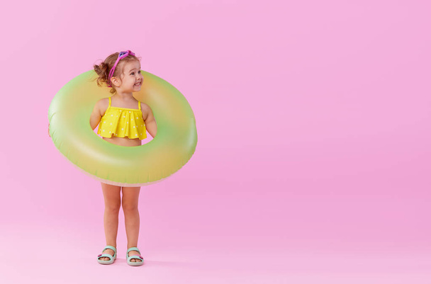 Portrait of happy little girl with neon inflatable rubber circle having fun isolated on pink background. Space for text on right side  - Фото, зображення