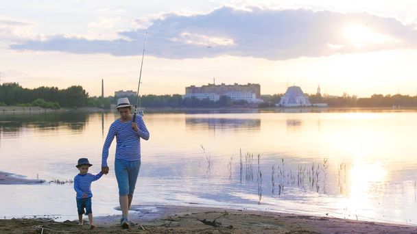 日没時に川に沿って行く釣り竿を持つ父と息子 - 写真・画像
