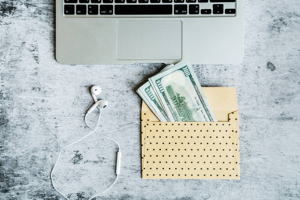 Desktop flatlay: laptop, one hundred dollars bills in envelope lying on gray marble background. Business, finance concept - Φωτογραφία, εικόνα