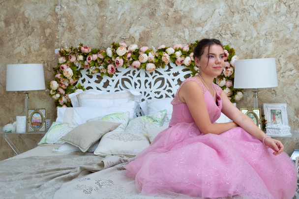Fashion portrait of young beautiful female model sitting in pink dress in interior studio. - Foto, afbeelding