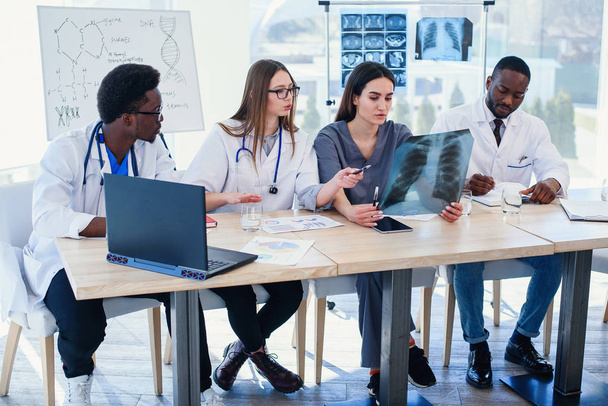 Group of doctors are studying disease patients history. Team of multiethnic young doctors having a meeting in conference room in the modern bright hospital. - 写真・画像