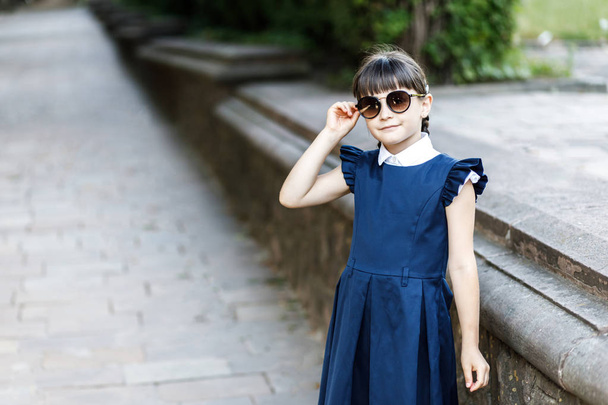 Ein süßes Schulmädchen amüsiert sich auf der Straße im Park. das Mädchen trägt Schuluniform - Foto, Bild