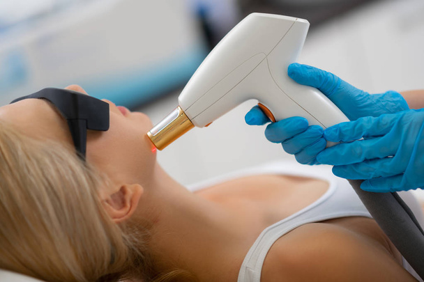 Косметолог проводит своему клиенту лазерное лечение лица
. - Фото, изображение