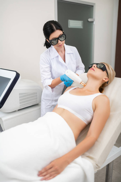 Beauty doctor giving her patient laser neck skin treatment. - Photo, image