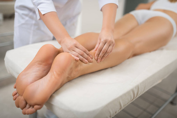 Cosmetologist massaging back side of calves of her client. - Fotó, kép