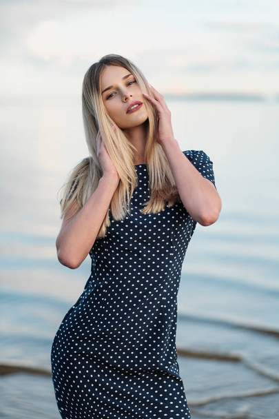 Portrait of young attractive blond woman, in a blue dress outdoors, hands on face. - Foto, Imagem