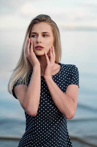 Portrait of young attractive blond woman, in a blue dress outdoors, hands on face. - Foto, imagen