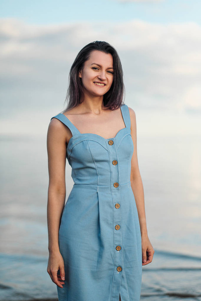 A young attractive dyed hair woman, in a blue dress, on background of seashore and sea. - Фото, зображення