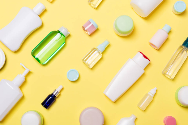 Vista superior de diferentes botellas de cosméticos y recipiente para cosméticos sobre fondo amarillo. Composición plana con espacio de copia
 - Foto, imagen