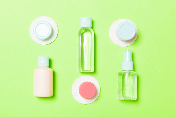 Set of travel size cosmetic bottles on green background. Flat lay of cream jars. Top view of bodycare style concept - Photo, Image