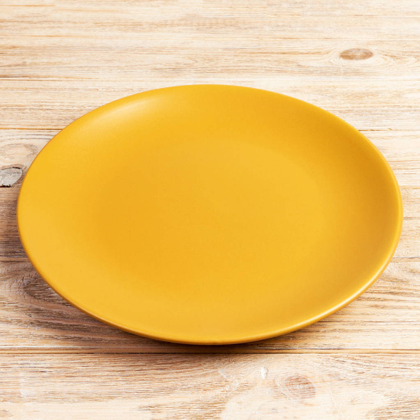 Gele ronde plaat op houten tafel achtergrond. Top View, sjabloon voor uw ontwerp - Foto, afbeelding