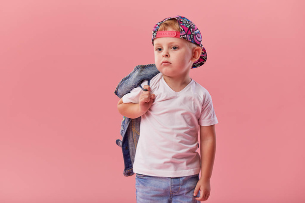 Little serious fashionable toddler boy in denim clothes and trendy cap on pink background  - Foto, afbeelding