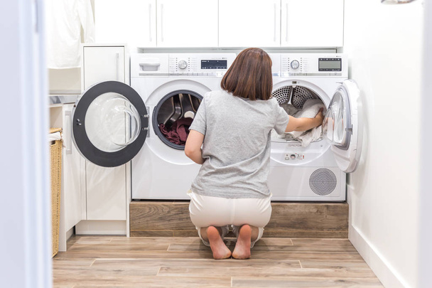 Nainen lastaus likaiset vaatteet pesukoneessa pesuun modernissa kodinhoitohuoneessa
 - Valokuva, kuva