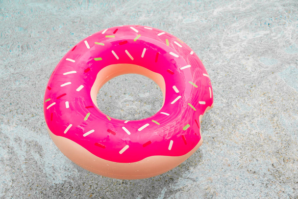 Anneau gonflable en caoutchouc flottant en forme de beignet rose dans l'eau de la piscine
 - Photo, image