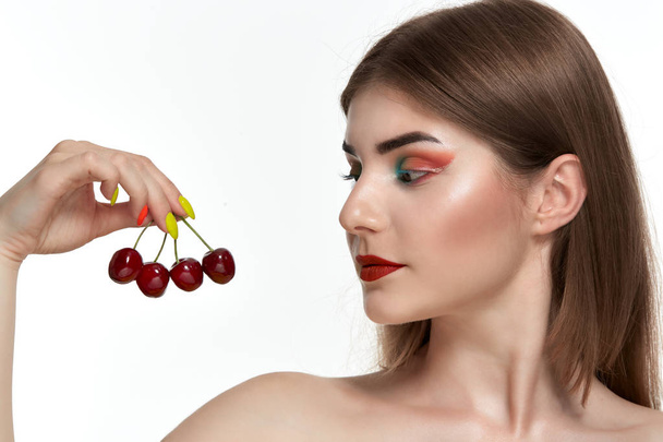 顔の近くにイチゴを保持する明るい色のメイクアップを持つ美しい若い女性のクローズアップ肖像画. - 写真・画像