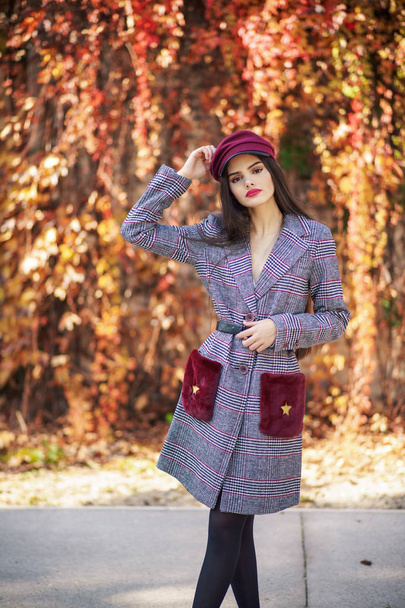 Молода красива дівчина в зимовому пальто і шапка на фоні осіннього листя
. - Фото, зображення