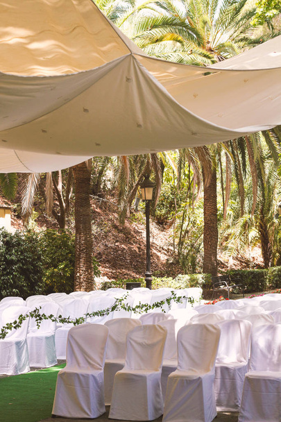 木陰の公園の外で結婚式のイベントでゲストのための白いケープの椅子の列, 天蓋の下のロマンチックな場所 - 写真・画像