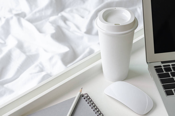 eine Tasse Kaffee neben Laptop und Maus mit weißem Tablett auf unordentlicher Decke. - Foto, Bild