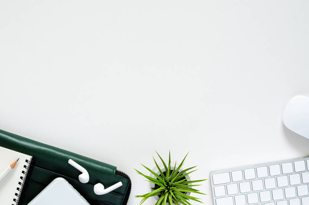 Modern workplace with wireless keyboard and mouse, smartphone with wireless earphones, pencil, notebook, green document bag and Tillandsia air plant on white background. - Fotografie, Obrázek