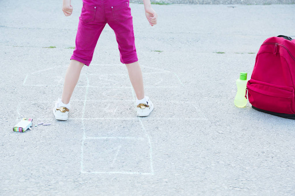 De vuelta a la escuela. Hermosa colegiala rubia jugando hopscotch dibujado con tiza de colores en asfalto fuera de la escuela primaria, concepto de educación
. - Foto, imagen