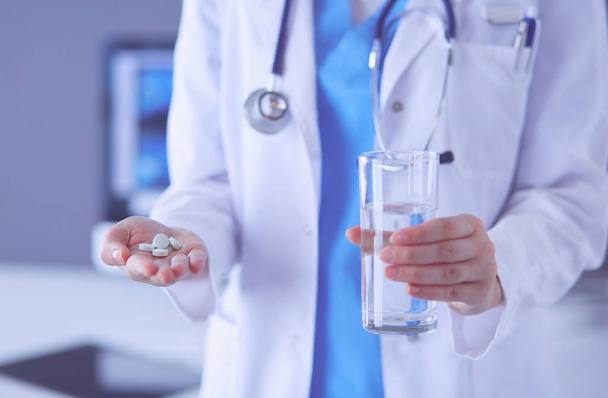shot of doctors hands holding pills and glass of water at clinic. - Фото, изображение