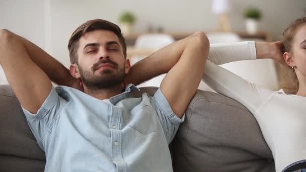 Couple putting hands behind head relaxing on sofa at home - Footage, Video