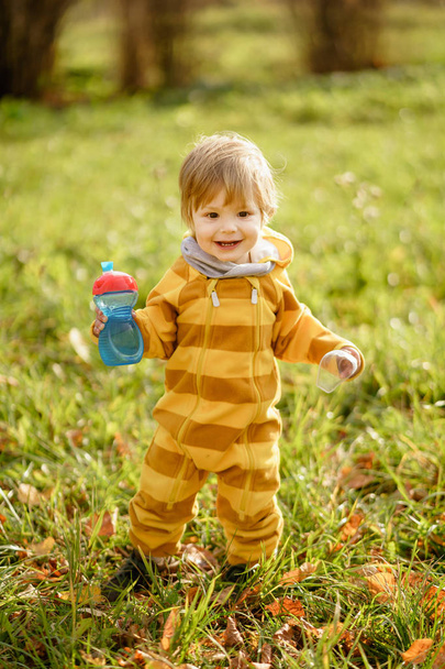 Ευτυχισμένο μικρό αγόρι με μπουκάλι νερού που παίζει το φθινόπωρο στο περπάτημα στο πάρκο - Φωτογραφία, εικόνα