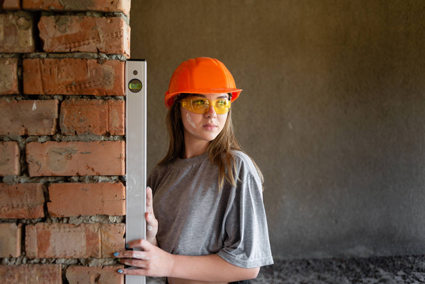 Genç bir kız mühendis duvarların eşitliğini ölçen bir seviyede. - Fotoğraf, Görsel