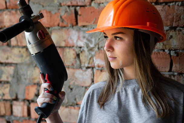 Une photo portrait d'une femme confiante dans un casque orange de construction avec une perceuse électrique à la main
. - Photo, image