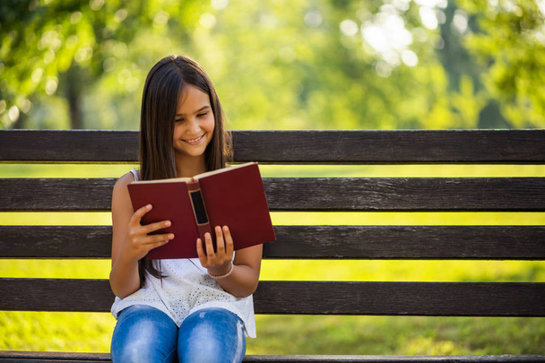 Happy little girl is reading a book in park. - Φωτογραφία, εικόνα