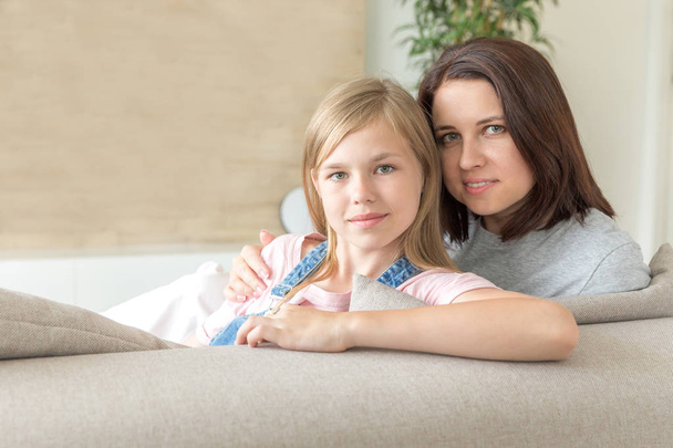 Mother and pre-teen daughter sitting on couch smiling. Happy family concept - Photo, image