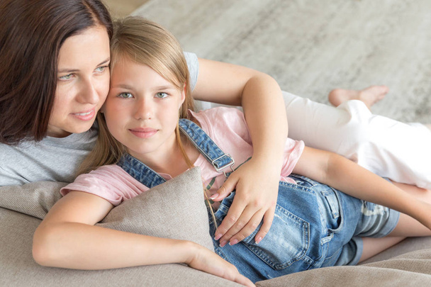 Mother and pre-teen daughter sitting on couch smiling. Happy family concept - Foto, imagen