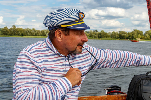 homem marinheiro em um boné em um barco sob a vela contra o céu e wat
 - Foto, Imagem