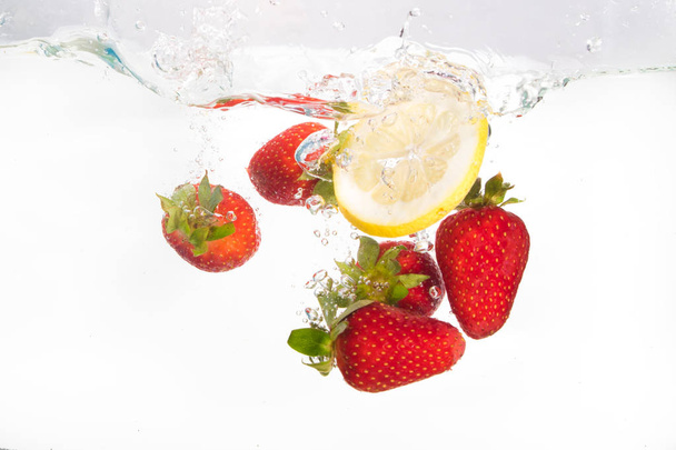 Strawberries and lemon slice splashing in to water on the white - Photo, Image