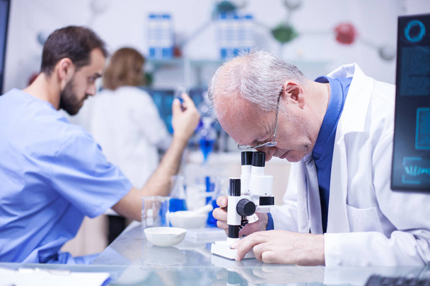 Scientifique senior portant un manteau blanc faisant une analyse avancée au microscope
 - Photo, image