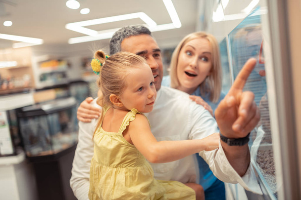 Daughter wearing yellow dress visiting pet shop with parents - Foto, afbeelding