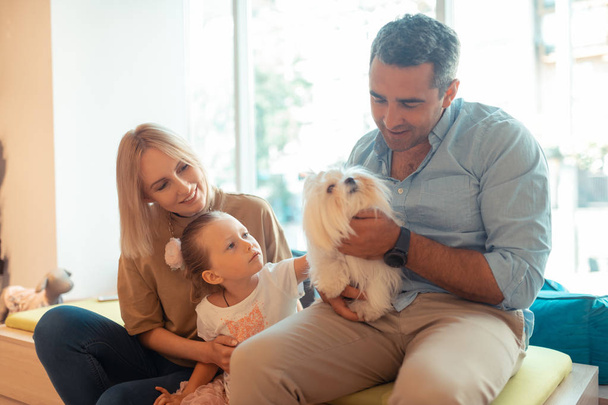 Father holding white fluffy dog sitting near wife and daughter - Foto, imagen