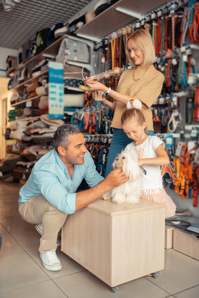 Mother choosing dog collar while dad and daughter playing with dog - Photo, Image