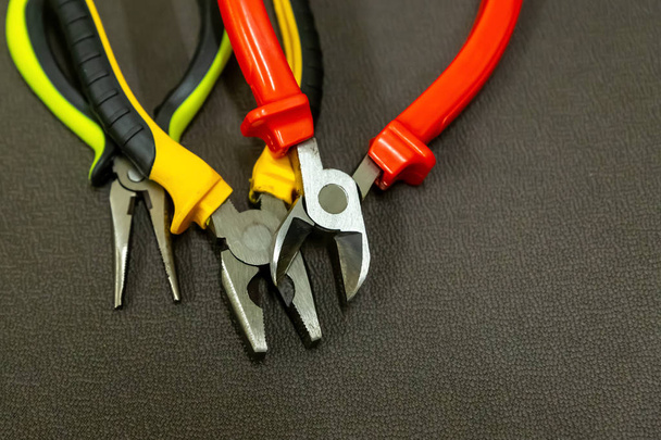 alicates abiertos herramientas de construcción con asas multicolores rojo amarillo sobre un fondo oscuro
 - Foto, imagen