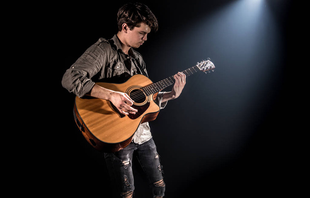 Guitarist, music. A young man plays an acoustic guitar on a blac - Foto, imagen
