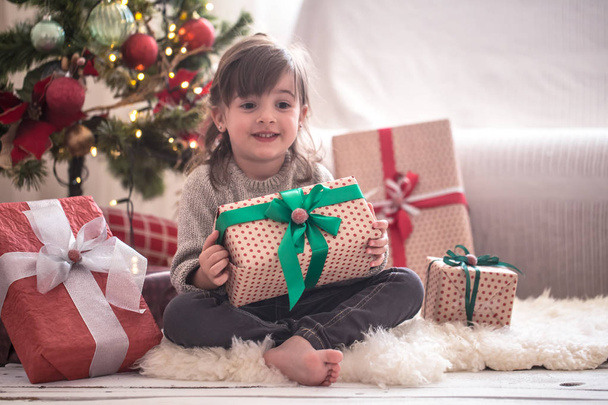 Menina bonita está segurando uma caixa de presente e sorrindo enquanto sitti
 - Foto, Imagem