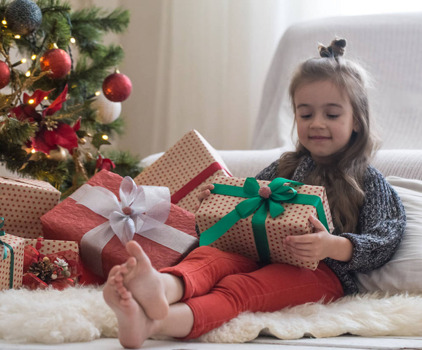 Bonita niña está sosteniendo una caja de regalo y sonriendo mientras sitti
 - Foto, imagen