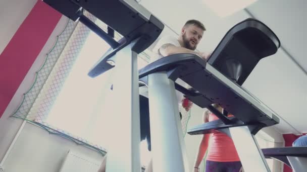 Guy runs on treadmill in fitness club. Weight loss drills from Individual instructor for fat man. Health and gym. Exercises and Practices. Warm up before the training by thick person. Personal coach - Materiał filmowy, wideo
